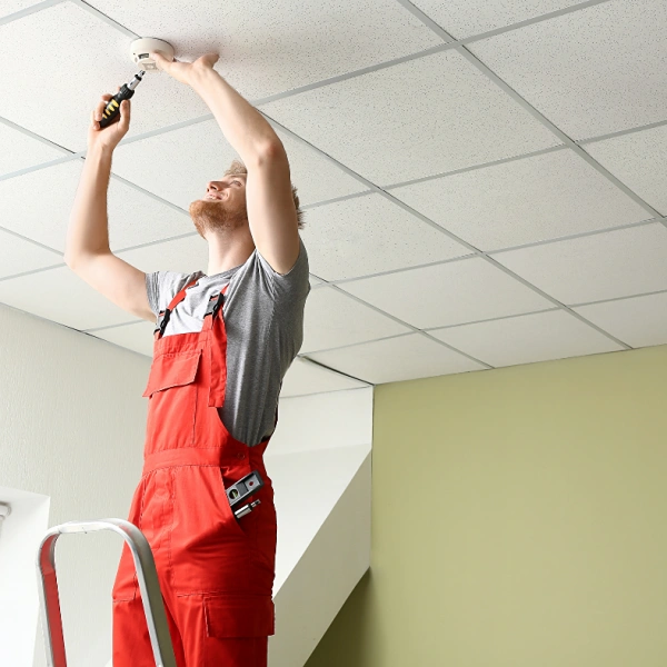 An engineer installing a fire detector on a ceiling