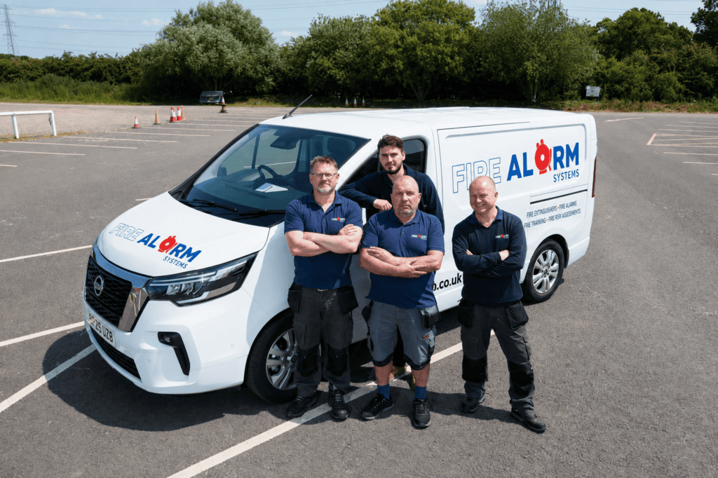 Four Fire Alarm Systems engineers standing in front of a branded company van