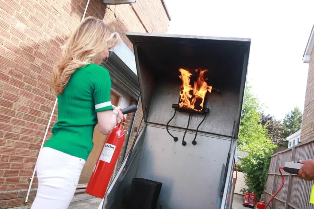 Woman using a fire extinguisher on a controlled fire in the live fire training unit during Fire Alarm Systems fire safety training